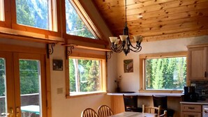 Una cabaña con amplios ventanales, techo de madera y una zona de comedor con sillas y una mesa.