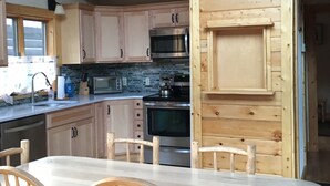 Un interior de madera con zona de cocina que incluye armarios, un microondas y una estufa. Hay una mesa de comedor con sillas.