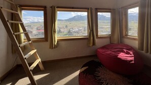 A room with a wooden ladder, a red bean bag, and multiple windows offering a mountain view.