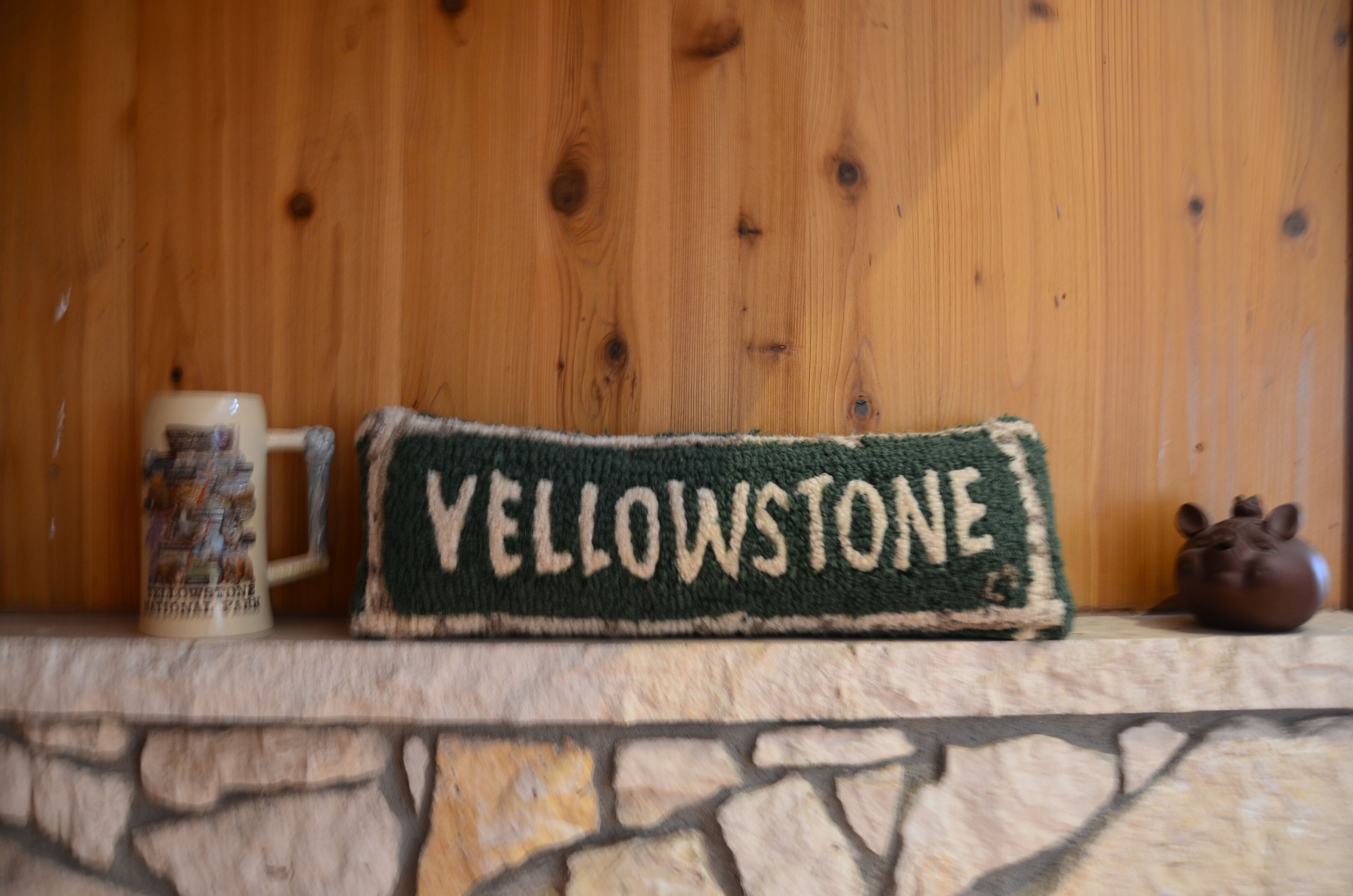 Una taza con diseño de Yellowstone, un tejido con el texto 'Yellowstone' y una pequeña figurina sobre una pared de piedra.