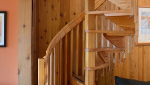 A wooden spiral staircase in a room with a wooden wall and a sofa.