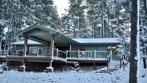 Een lodge met een overdekt terras en een stenen fundering, omringd door met sneeuw bedekte bomen.