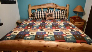 Een bed met een houten hoofdbord, een ruitendekbed met dierenprint en een nachtkastje met een lamp.