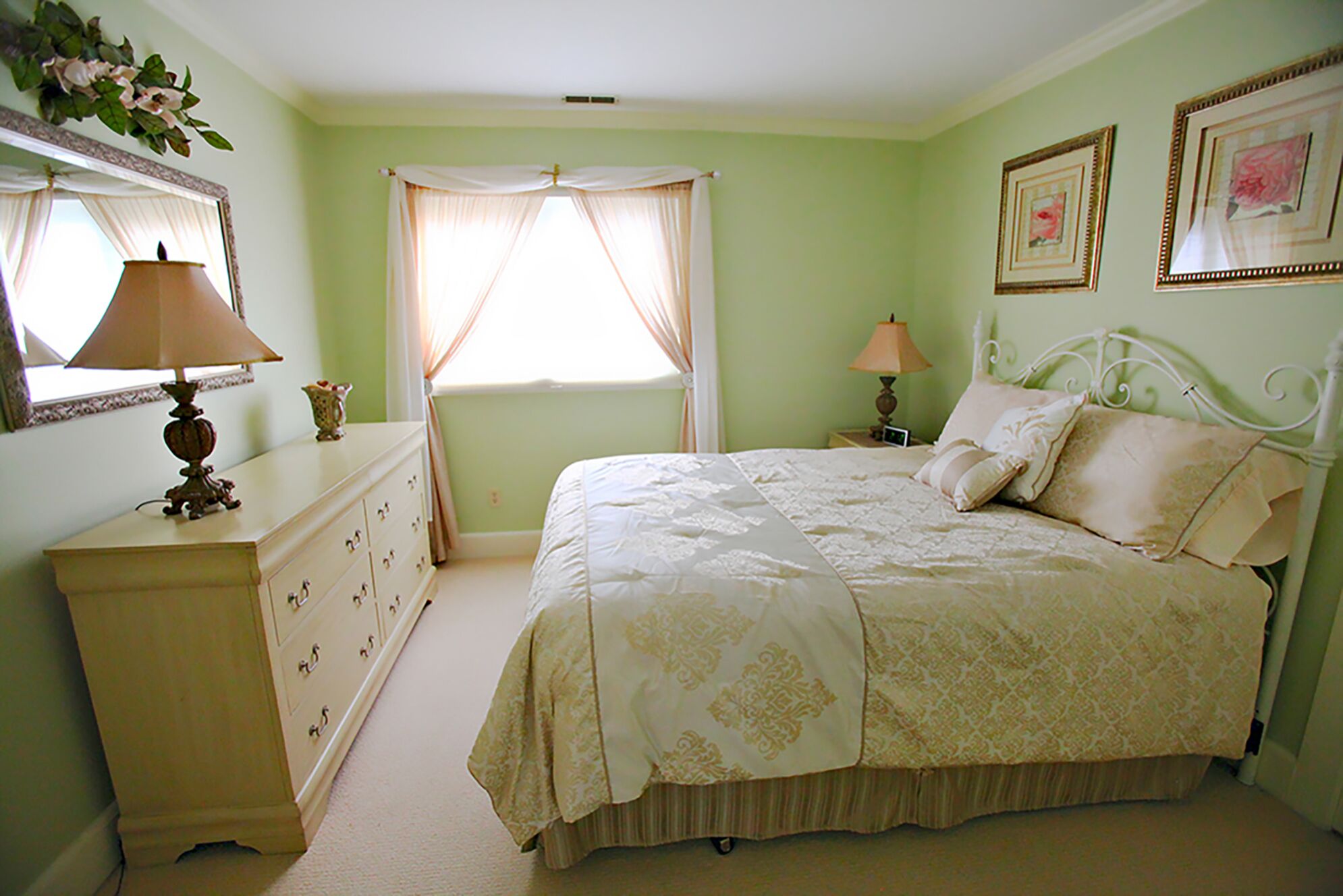 Um quarto com cama, cômoda, mesa de cabeceira, abajur e quadros na parede.