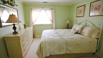 Um quarto com cama, cômoda, mesa de cabeceira, abajur e quadros na parede.