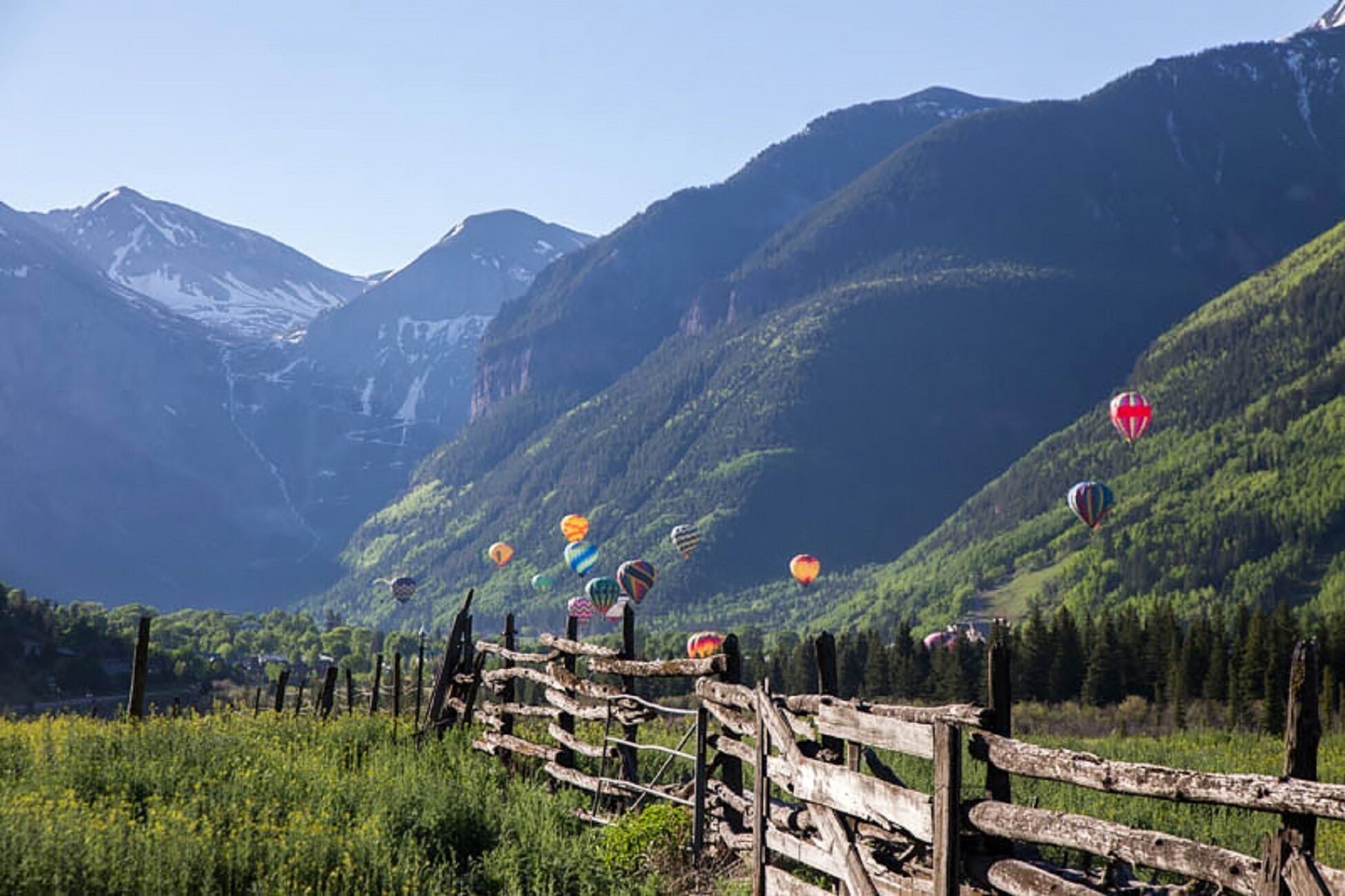 A mountainous landscape with a wooden fence and hot air balloons in the distance.