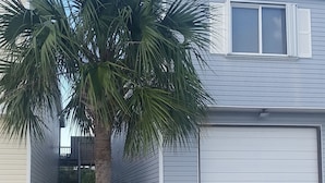 A residential garage with a closed white door, a palm tree in front, and a wooden fence. - LP1A is a Great Coastal Condo in the heart of Port Aransas (Port Aransas)