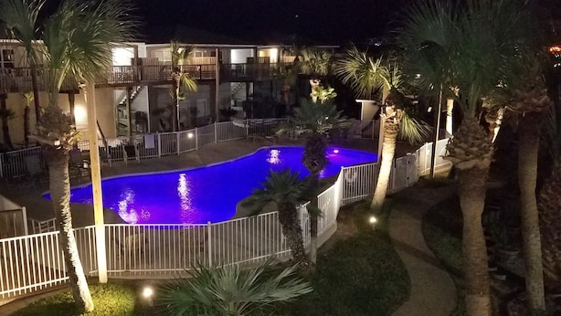 A swimming pool with a blue light, surrounded by palm trees and a fenced area. - LP1A is a Great Coastal Condo in the heart of Port Aransas (Port Aransas)