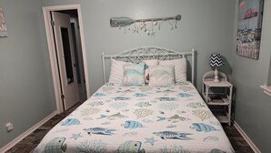 A bedroom with a bed, pillows, a nightstand, a lamp, and a wall decoration. - LP1A is a Great Coastal Condo in the heart of Port Aransas (Port Aransas)