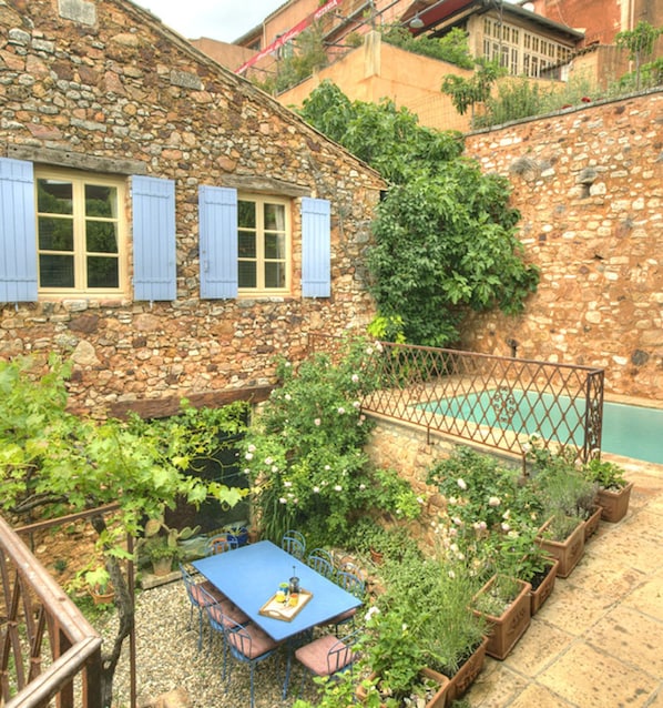 A stone building with a pool, a table with chairs, and potted plants.