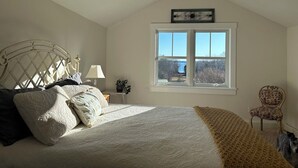 Een slaapkamer met een bed, een raam, een stoel en een lamp.