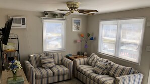 A living room with two striped sofas, a wooden coffee table, a rug, a ceiling fan, and a window with blinds. - Charming Beach block getaway! Leave your sheets, towels at home! You're on VACA! (Brigantine)