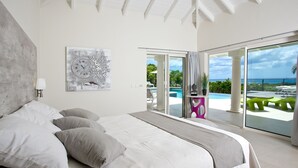 Un dormitorio moderno con una cama grande, vistas a la piscina y al océano, y una obra de arte contemporánea en la pared.