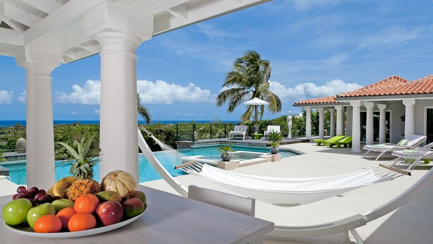 Zona junto a la piscina con vista al océano, una mesa con fruta y sillones de descanso.