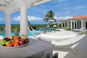 A poolside area with a view of the ocean, a table with fruit, and lounge chairs. - OCEAN VIEW MODERN AND DESIGN VILLA (Terres Basses)
