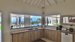 Una cocina con armarios de madera, un fregadero y vista a una piscina y palmeras.