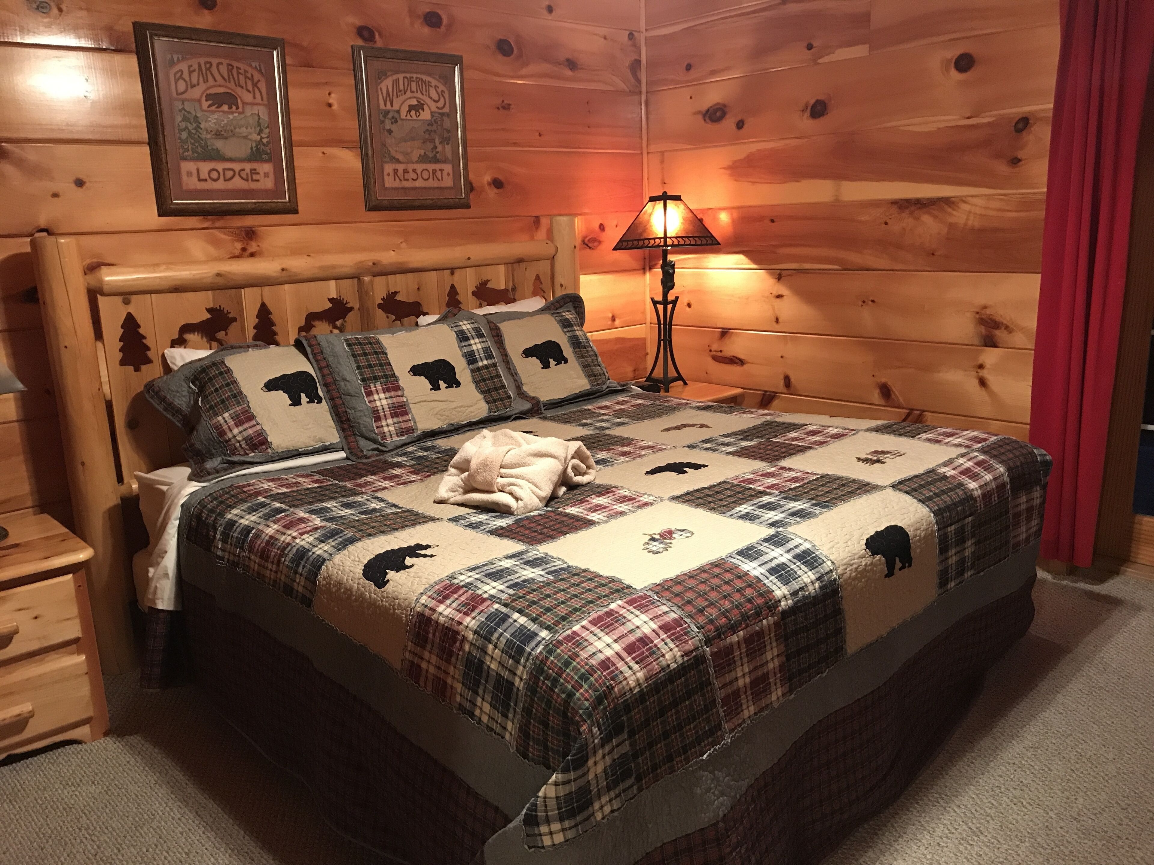 Een gezellige kamer met een houten hoofdbord, een gewatteerde plaid met berendesigns, een bedlampje en twee ingelijste borden aan de muur.