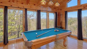 A pool table in a wooden room with large windows and a view of trees. - Free Tickets | Secluded Spacious Cabin w/Mountain View, Hot Tub & Game Room (Sevierville)