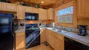 A compact kitchen with wooden cabinets, a black refrigerator, a microwave, a stove, a sink, and a coffee maker. - Free Tickets | Secluded Spacious Cabin w/Mountain View, Hot Tub & Game Room (Sevierville)