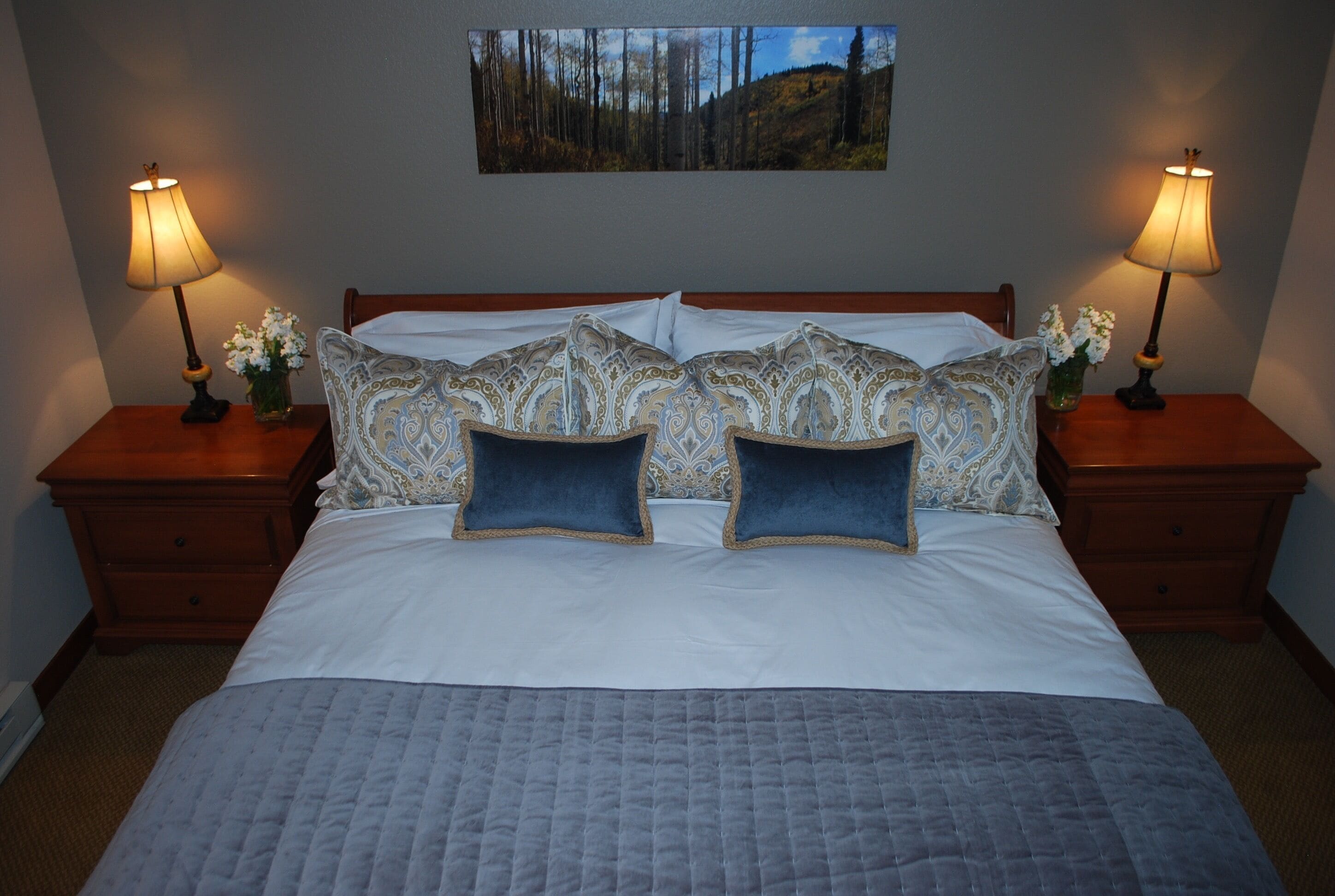 A neatly made bed with patterned pillows, two bedside tables with lamps, and a framed picture on the wall.