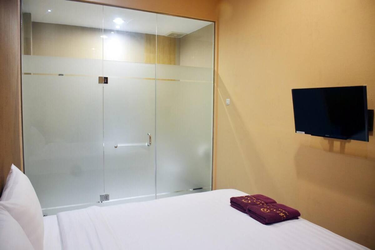 A hotel room with a bed, a glass-enclosed wardrobe, and a mounted television.
