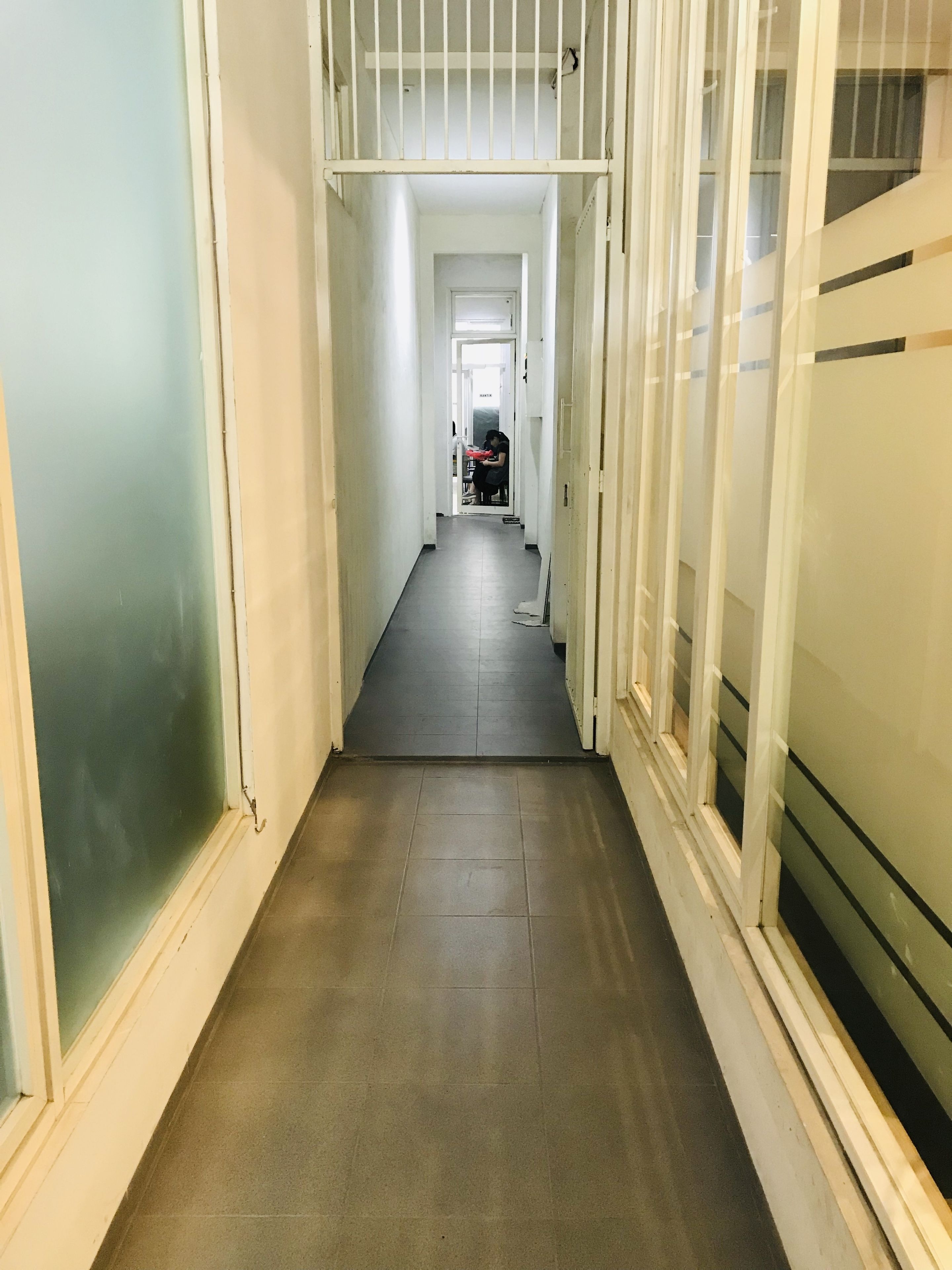 A narrow hallway with a tiled floor leading to a room with a bed and a window.