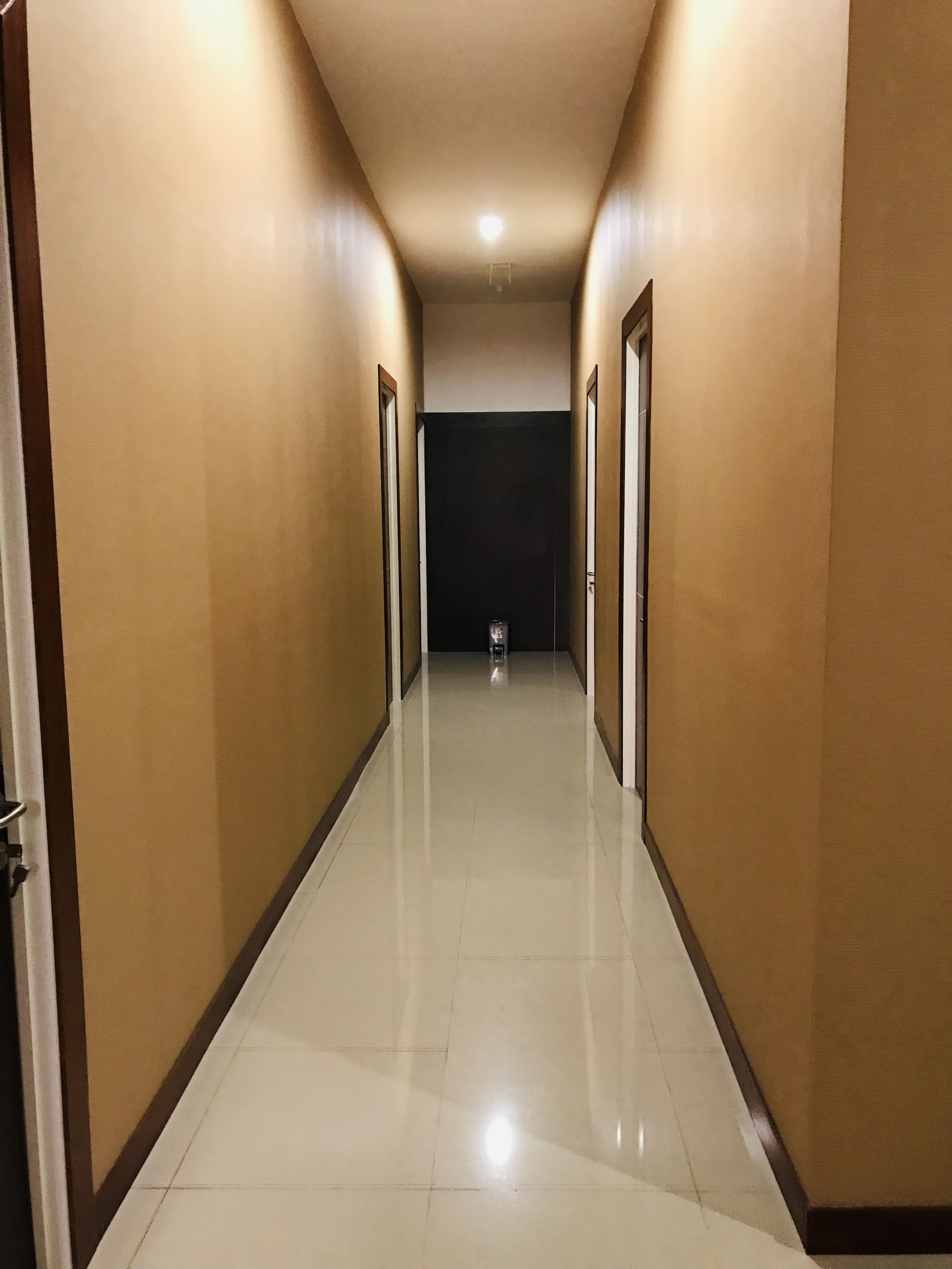 A long, narrow hallway with beige walls and a shiny tiled floor, leading to a dark room at the end.