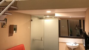 A modern interior with a red sofa, a glass door, a white sink, and a staircase leading to an upper level. - Great Star Premium Homestay (Malang)