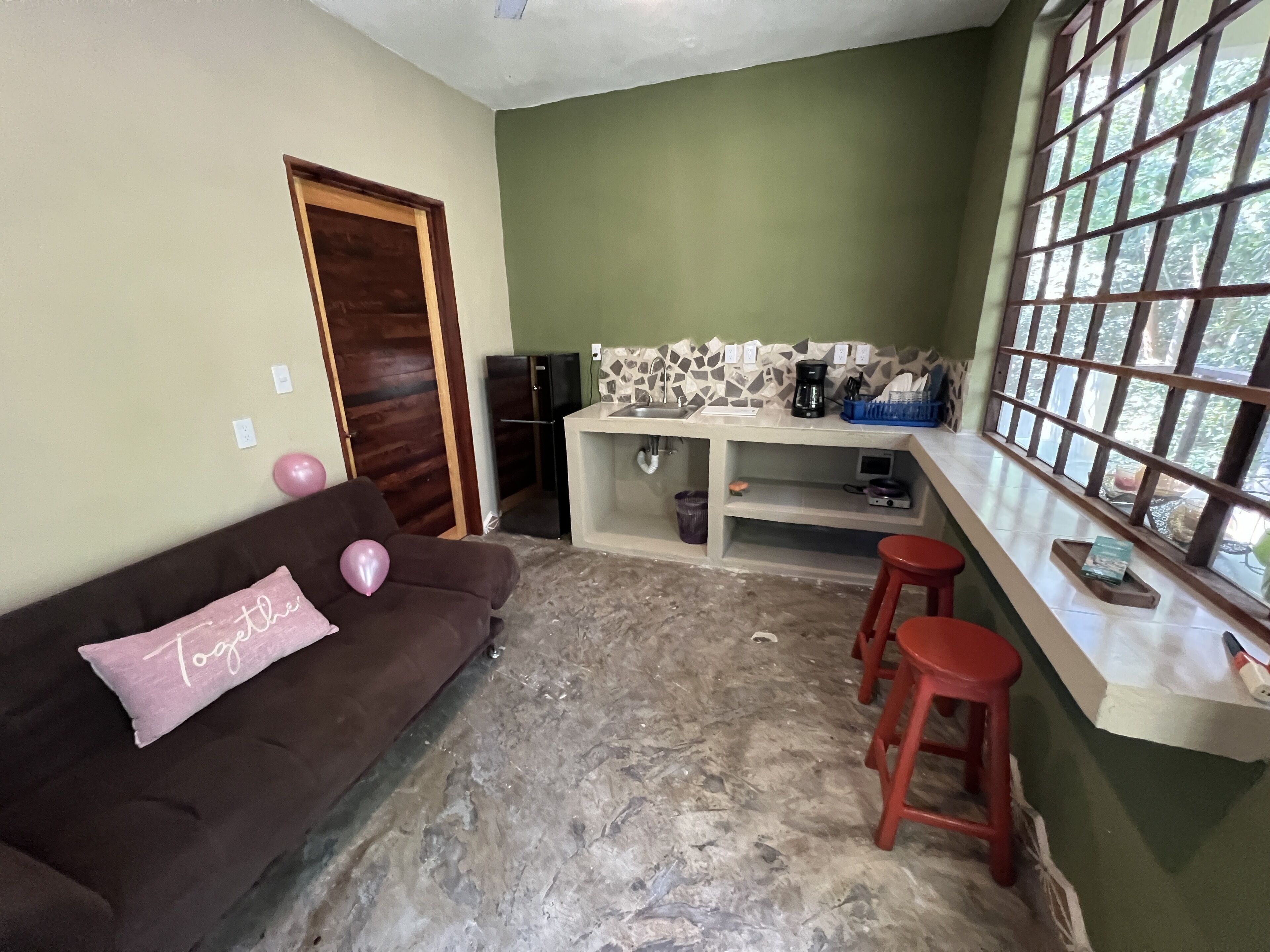 Una cocina compacta con refrigerador, cafetera y ventana con vista a follaje.