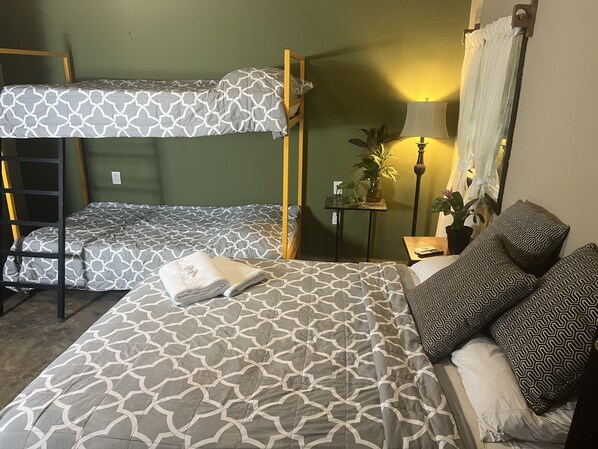 Ein Schlafsaalzimmer mit Etagenbetten, einem Nachttisch mit Lampe, einem Topf mit Pflanze und einem Spiegel.