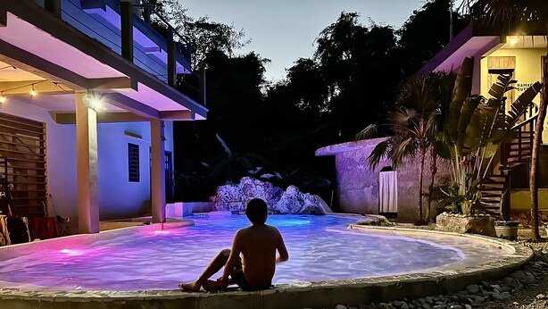 A person sitting by a pool at night, surrounded by a modern house with a stone pathway and tropical plants. - Hokhmah Heart Hotel (Puerto Morelos)