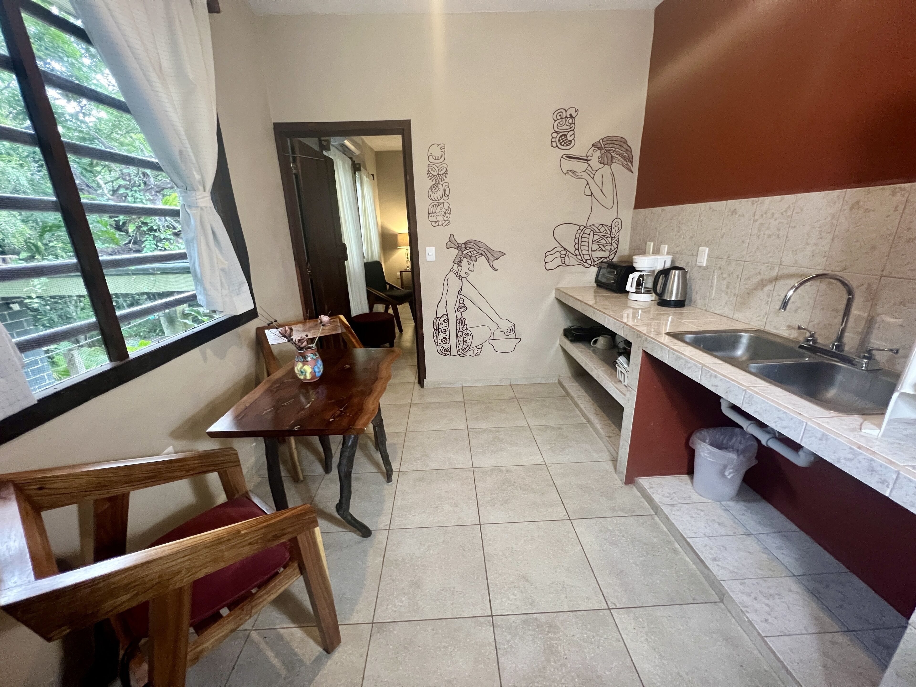 A compact kitchen with a dining area, a sink, and a window with curtains.