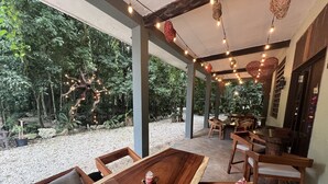 An outdoor dining area with a wooden table and chairs, surrounded by greenery and a covered structure with string lights. - Hokhmah Heart Hotel (Puerto Morelos)