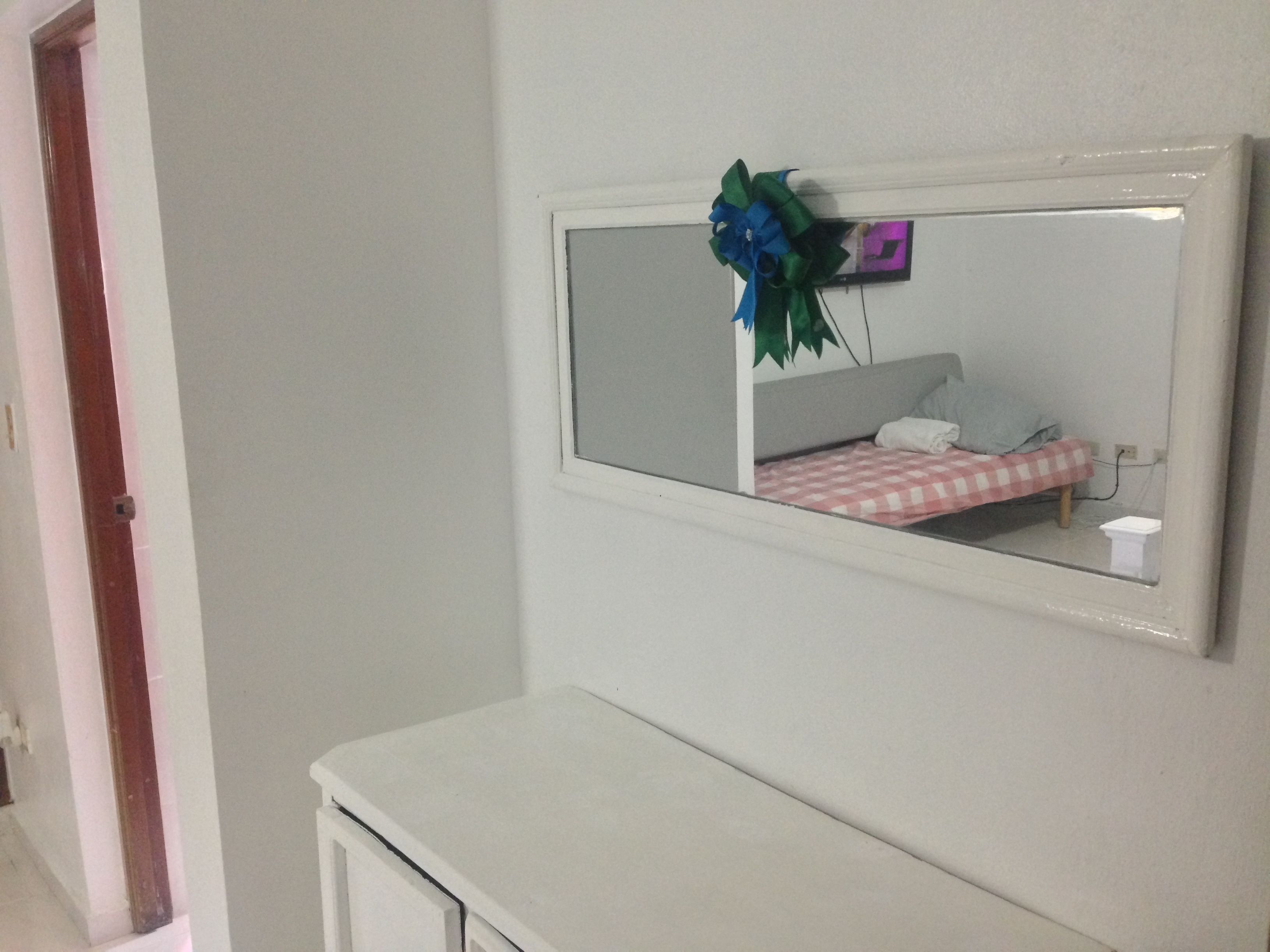 Une chambre à coucher avec un lit, une table de chevet et un miroir orné d’un nœud décoratif.