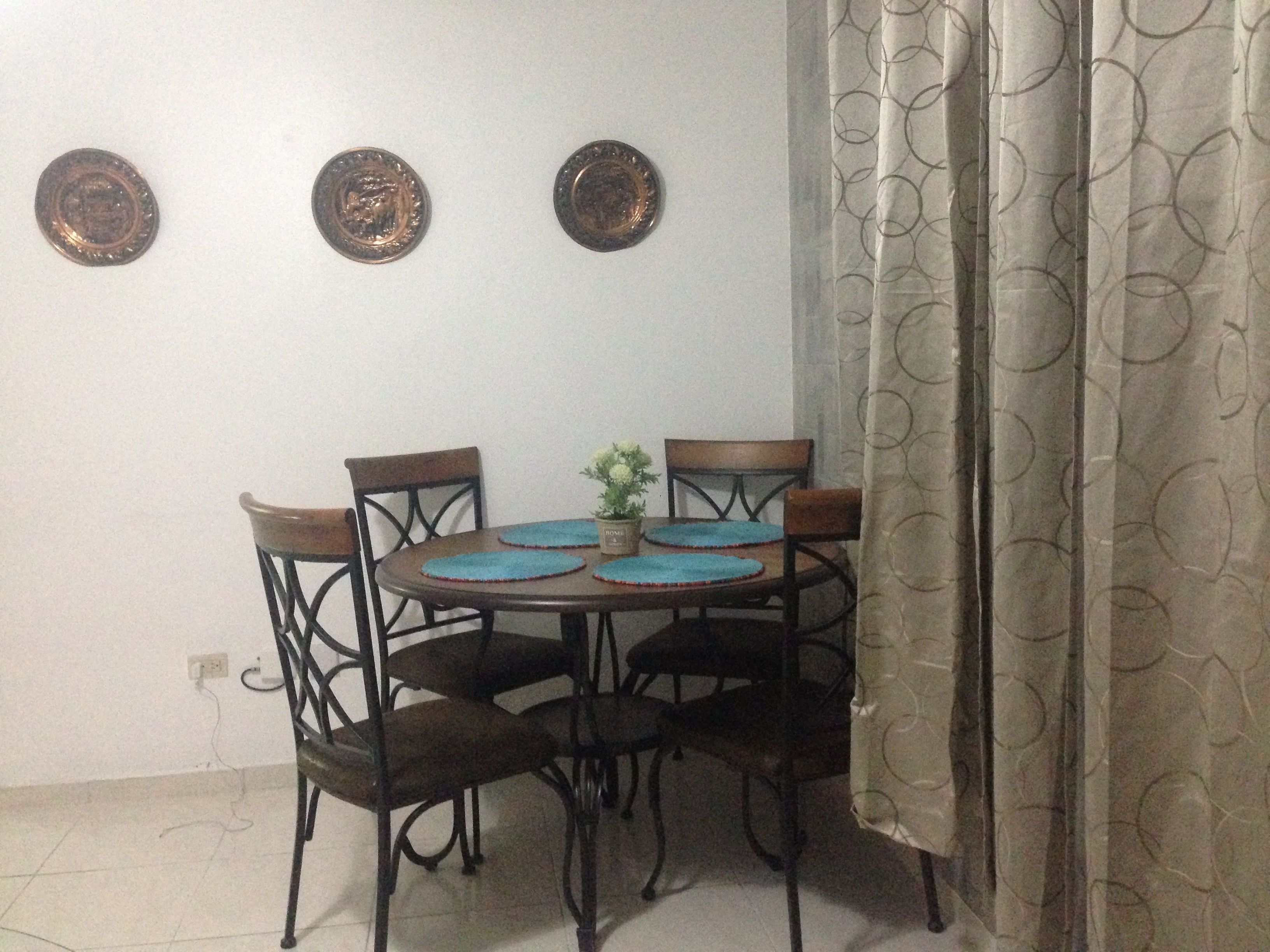 Een eethoek met een ronde tafel, vier stoelen en drie decoratieve borden aan de wand.