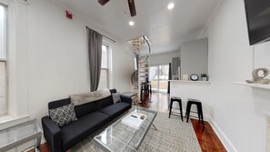 A modern living room with a black sofa, a glass coffee table, and a staircase leading to an upper level. - TheU-BnB (Philadelphia)
