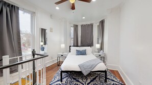 Un dormitorio moderno con cama, mesitas de noche, ventilador de techo y vistas al exterior.