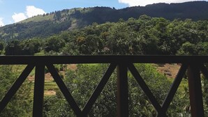 Vista desde un balcón cubierto con estructura metálica, sobre un paisaje verde y exuberante con campos escalonados y una colina al fondo.