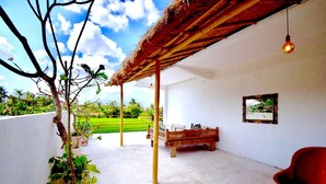 Una habitación con techo de paja, una cama, una silla y un cuadro en la pared.