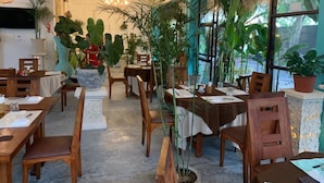 Un restaurante con mesas y sillas de madera, plantas en macetas y un candelabro.