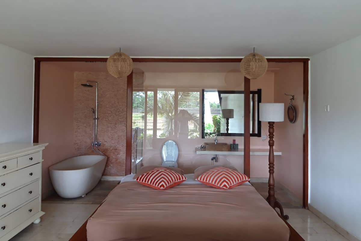 A bedroom with a large bed, a bathtub, a dresser, and a window with a view of greenery.
