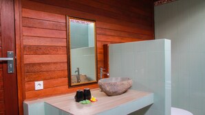 A bathroom with a wooden wall, a large mirror, a stone sink, and a toilet. - Bukit Permata Lembongan (Lembongan Island)