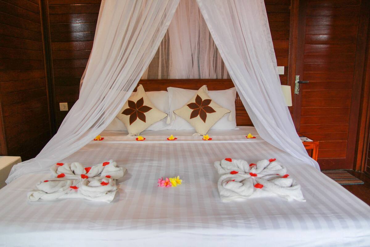 A bed with a canopy, white pillows with brown floral patterns, and towels arranged on the bed.