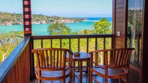 A wooden deck with two chairs and a table, overlooking a coastal view with turquoise waters and a distant shoreline. - Bukit Permata Lembongan (Lembongan Island)