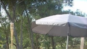 A person seated at an outdoor table with a canopy, holding a book and a glass.