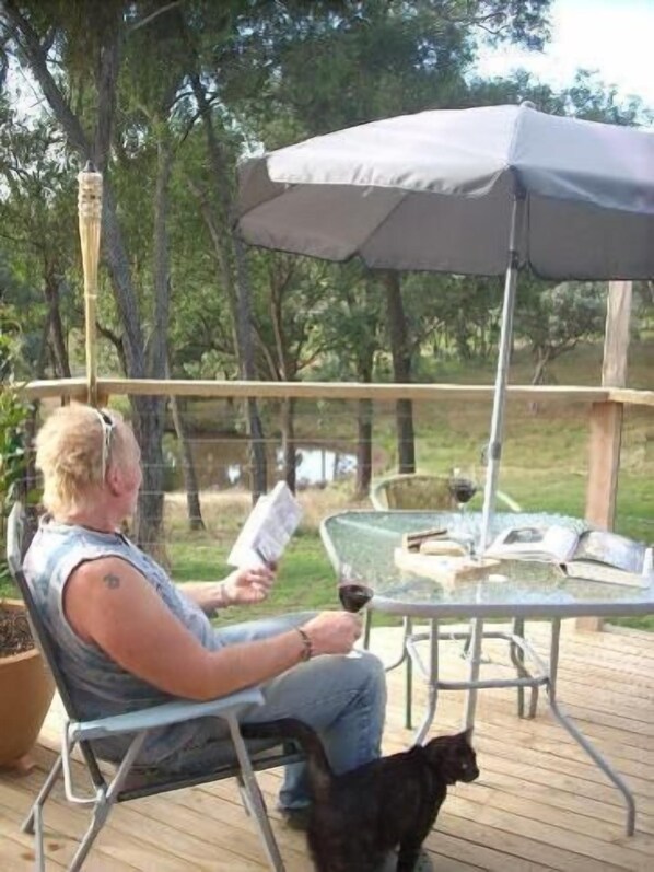 A person seated at an outdoor table with a canopy, holding a book and a glass.
