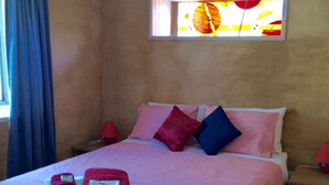 A hotel room with a bed, pillows, a nightstand, a window with a view, and a red lamp.