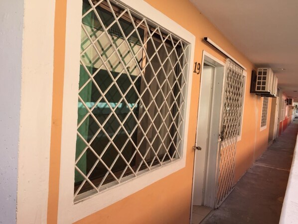 Guest rooms line this secure corridor with numbered doors and metal grilles on the windows.