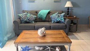 Un salon avec un canapé gris, des coussins décoratifs, une table basse en bois et des œuvres d’art murales.