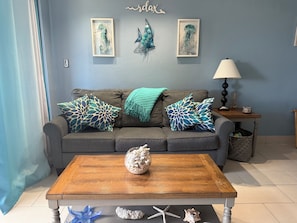 Un salon avec un canapé gris, des coussins décoratifs, une table basse en bois et des œuvres d’art murales.
